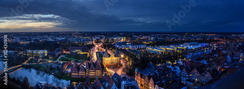 Luebeck, Germany – December 17, 2019: Aerial night view panorama, illuminated city of Luebeck in winter with Holstentor, Salzspeicher and river Trave, long exposure at blue hour, copy space