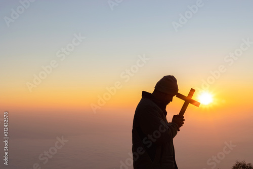 Human praying and holding christian cross for worshipping God at sunset sky background.Christian, Christianity, Religion copy space background. © AungMyo