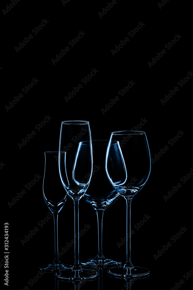 Glassware selection with wine, champagne and liquour glasses toned in classic blue on the dark background.. Fine cristal glassware concept. Vertical