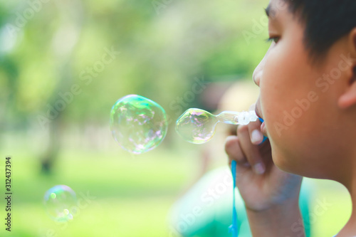 An Asian boy is playing blowing bubbles. At the park