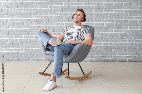Handsome man listening to music while sitting in armchair near grey wall © Pixel-Shot