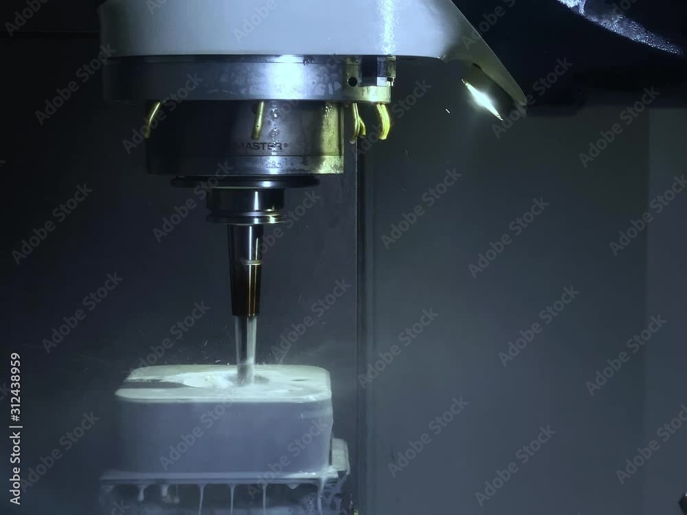 CNC Fräsmaschine bearbeitet unter Kühlmittel / Emulsion einen Metallblock aus Edelstahl