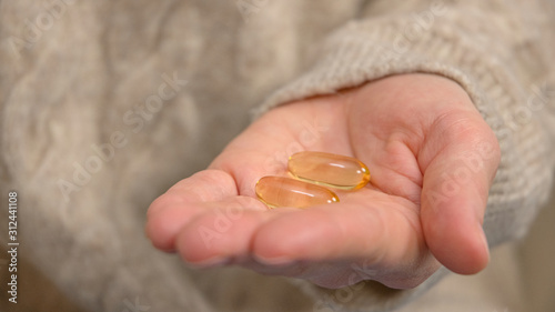 Fish oil capsules. Woman is holding Omega 3 into the palm of her hand.