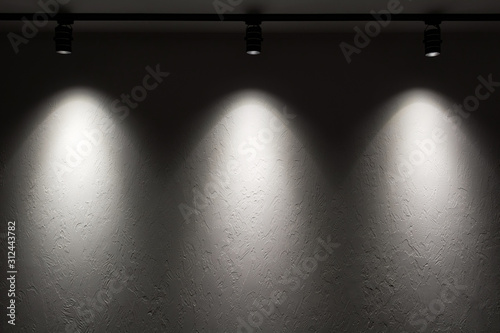 White wall with track light. Spotlight beams on the wall. Dark background. photo