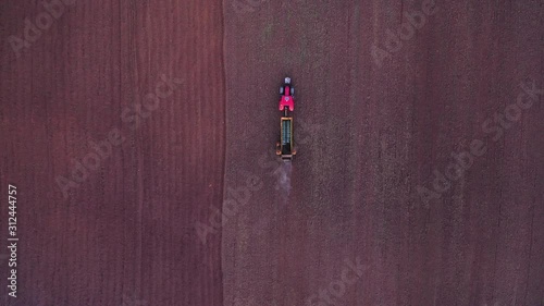 AERIAL: Descending Follow Shot of Red Tractor Spreading Manure on the Field in Evening, Manure Intended for Land Fertilizer Before Planting the Crop photo