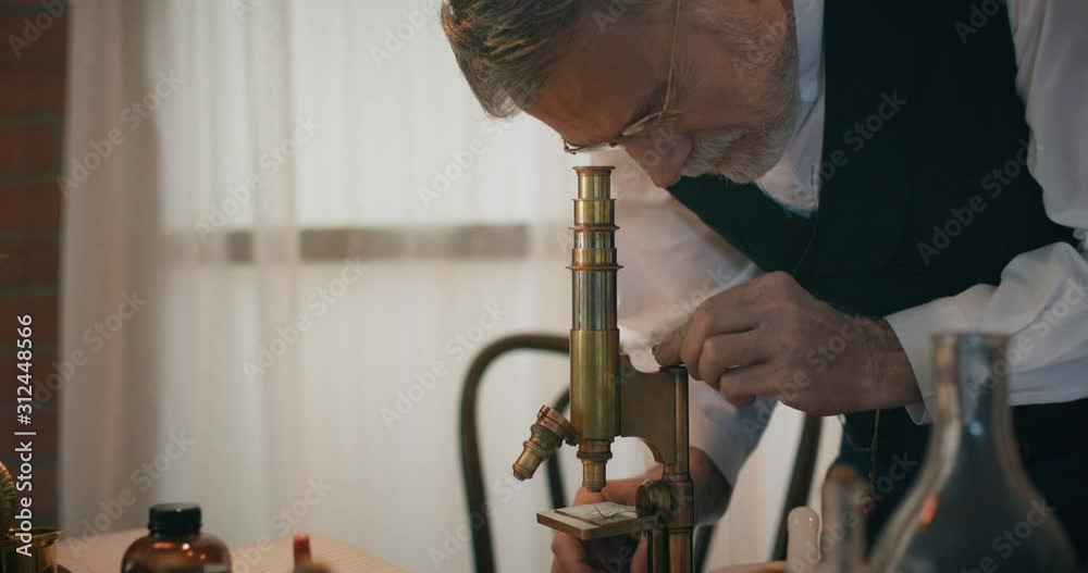Observation Using Microscope Vídeo do Stock: Tilt down from a 1898 scientist looking into a ...
