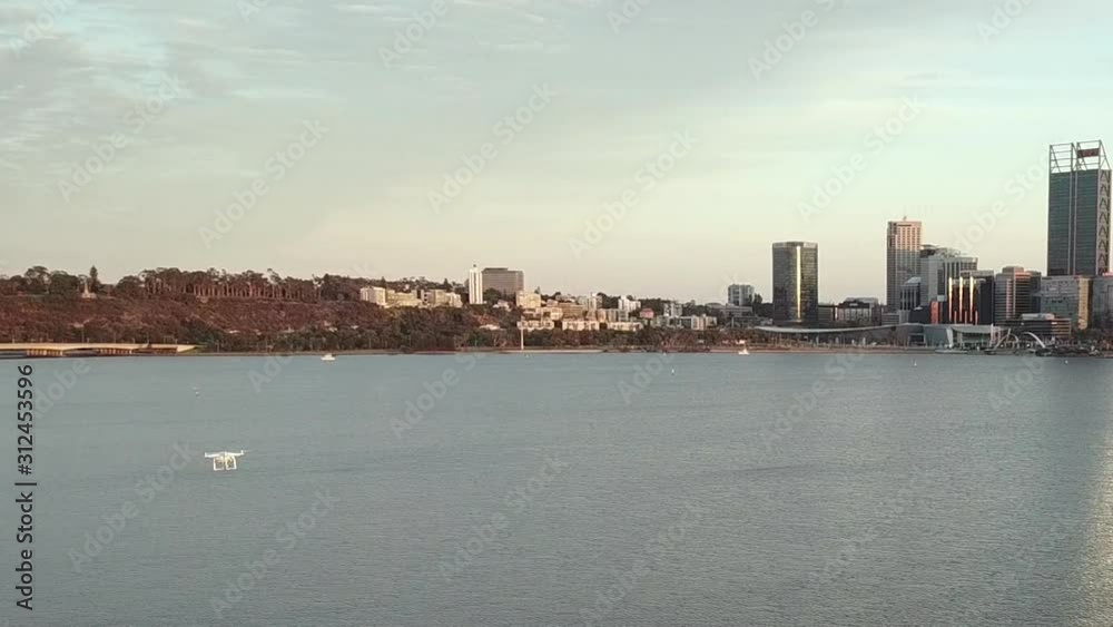 Aerial of white drone flying over water towards city skyline, early morning, tracking shot Aerial of white drone flying over water towards city skyline, early morning, tracking shot