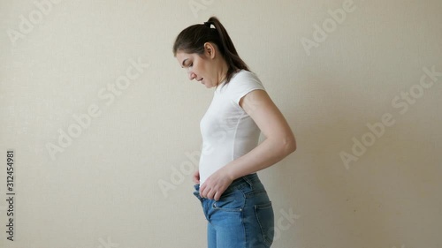 brunette woman struggles to button her jeans. Side view. photo