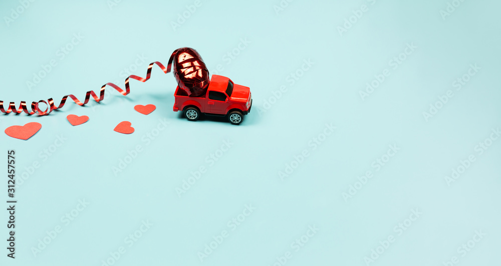 Fototapeta premium Valentines Day Theme Concept. Retro red toy car with red carnival serpentine and red heart confetti on mint background. Copy Space.