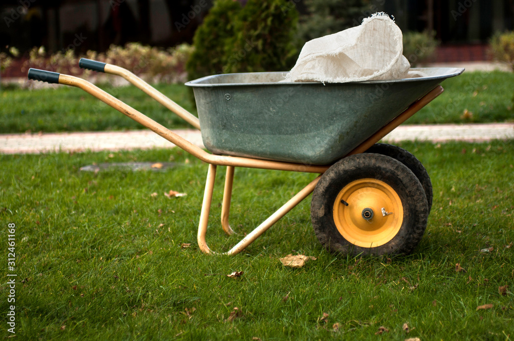 Naklejka premium A wheelbarrow with a sack for trash/ soil/ mulch/ compost/ fall leaves. Agricultural or landscaping works at backyard or park.