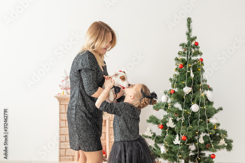 Holidays and pet concept - mother and daughter playing with jack russell terrier dog in front of christmas tree at home