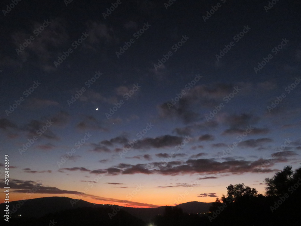 Naklejka premium moon and first star in sun set sky over mountains