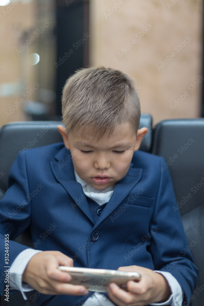 The boy uses the phone and plays games. Children are interested in online games and cartoons. A schoolboy in a school uniform and plays on a smartphone after school The boy uses the phone and plays games. Children are interested in online games and cartoons. A schoolboy in a school uniform and plays on a smartphone after school