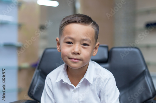 Close-up portrait of an attractive handsome smiling boy looking at camera after a haircut on white shirts. Beautiful boy. Six year old boy smiling and having fun