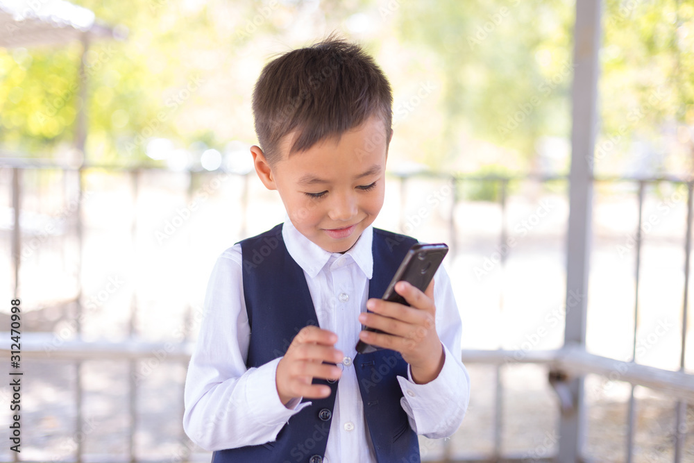 A boy in a school uniform holds a smartphone, talking loudly