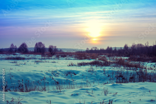 Winter landscape. Evening in the countryside. Sunset with beautiful gradient sky in the field covered with snow. Rural landscape with magical light.