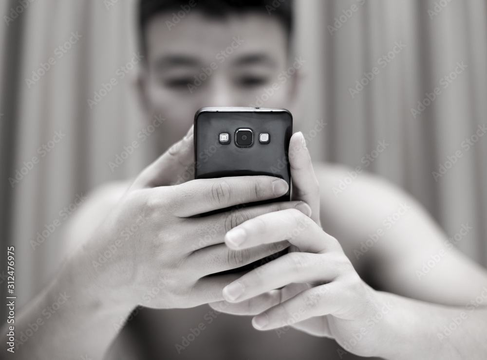 Handsome casual young man sitting at home, reading a sms on his mobile phone with a smile Handsome casual young man sitting at home, reading a sms on his mobile phone with a smile
