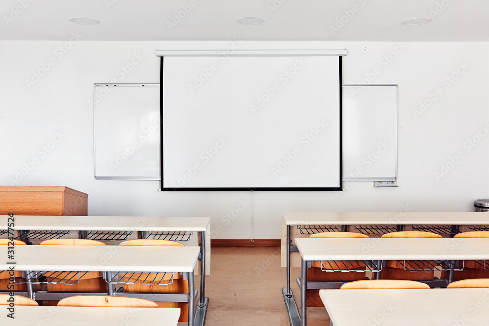 Classroom interior with projection screen, white board and wooden desks ...