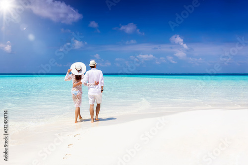 A hugging honeymoon couple walks down a tropical beach with turquoise sea and sunshine  photo