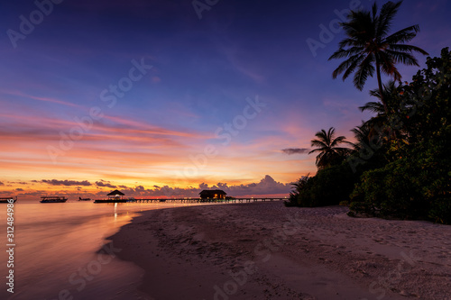 Sonnenuntergang über einer tropischen Insel mit Palmen und einsamen Strand auf den Malediven