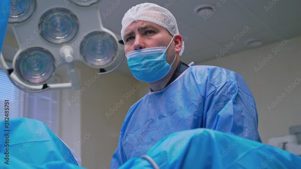 Portrait of a surgeon looking seriously. Medical specialist in a uniform and mask during the complicated surgery in modern operating room.