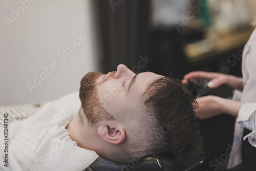 Barber washes the hair of a bearded client in a barbershop