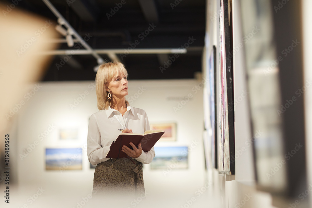 Waist up portrait of elegant mature woman looking at paintings in art gallery hall and enjoying museum exhibition, copy space Waist up portrait of elegant mature woman looking at paintings in art gallery hall and enjoying museum exhibition, copy space
