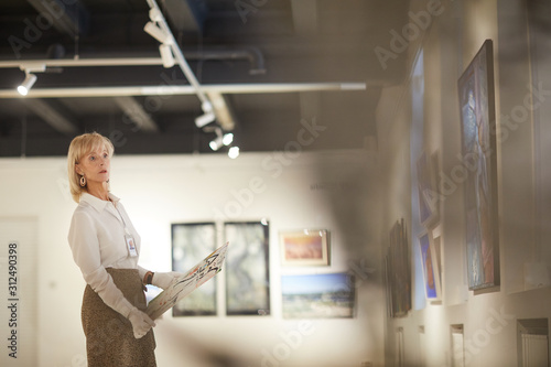 Wide angle portrait of female art expert appraising paintings in modern gallery or museum  copy space