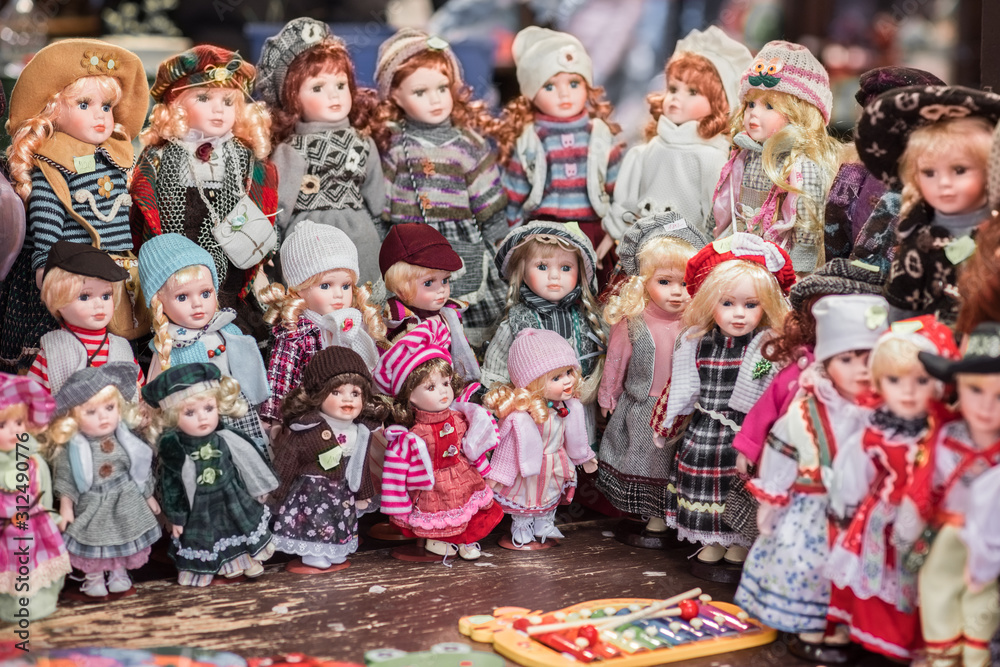 Naklejka premium Group of mainly young blond hair women in hats, caps beanies and autumn winter fashion clothes - crowd of baby toys - large collection of attractive girls dolls standing on Christmas flea market stand
