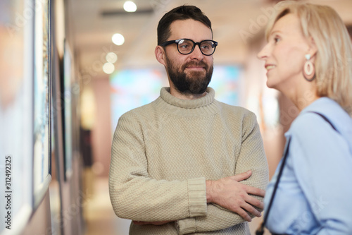 Waist up portrait of smiling bearded man looking at wife while enjoying exhibition in art gallery or museum