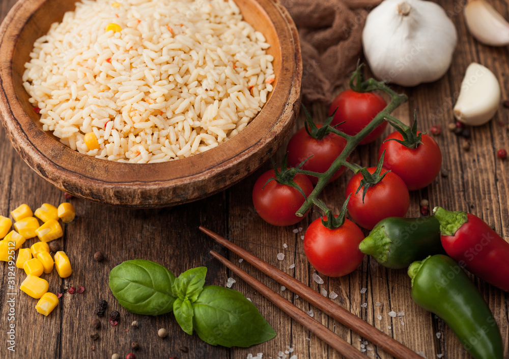 Wooden bowl with boiled long grain basmati rice with vegetables on wooden table background with sticks and tomatoes with corn,garlic and basil. Macro Wooden bowl with boiled long grain basmati rice with vegetables on wooden table background with sticks and tomatoes with corn,garlic and basil. Macro