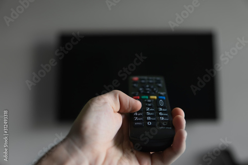 The man with the remote control in hand want switch on the TV and presses the button on the remote control. Remote control in hand closeup.