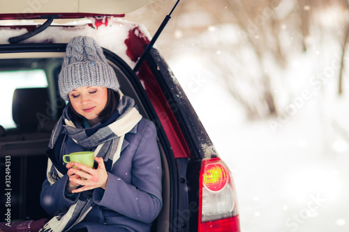 Caucasian woman with hot mug in car trunk winter