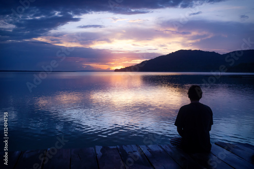 Man sitting on dock with orange sunset on purple blue sky along lake Itza, El Remate, Peten, Guatemala © Loes Kieboom