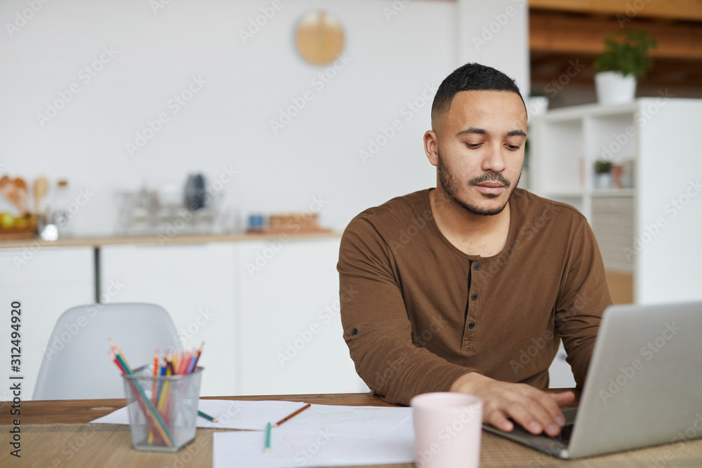 Portrait of modern mixed race man using laptop while working in home interior, copy space - obrazy, fototapety, plakaty 
