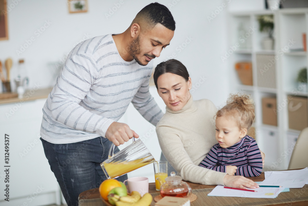 Portrait of happy mixed-race family drinking orange juice while enjoying morning together at home, copy space