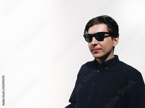 Young funny handsome guy in sunglasses at white wall at background