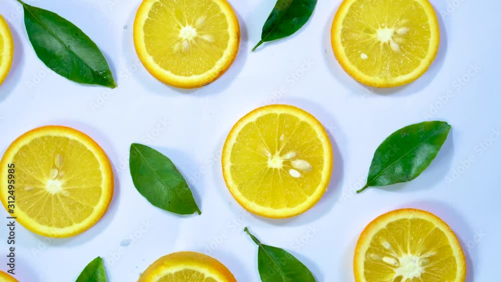 top angle rotating shot of orange slices and fresh orange leafs in a pattern on white background top angle rotating shot of orange slices and fresh orange leafs in a pattern on white background