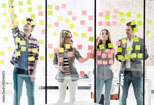 Group of creative business people writing plans on adhesive notes in office