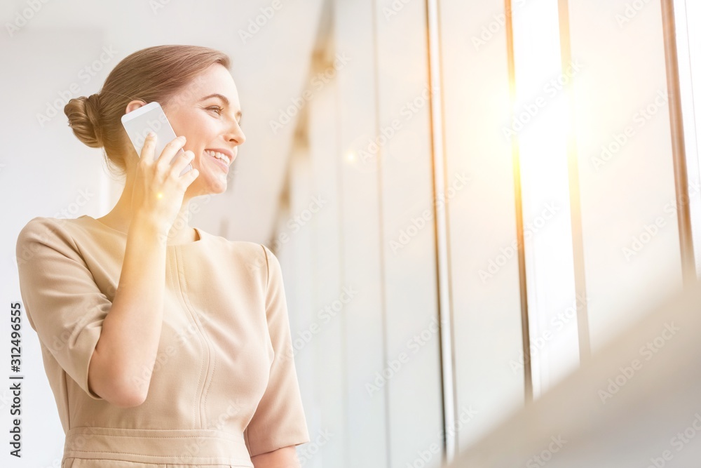 Smiling young businesswoman talking on smartphone while standing at new office