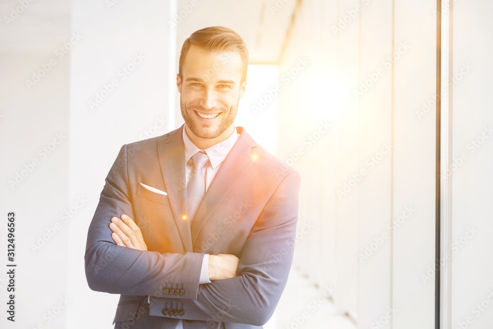 Portrait of smiling handsome young businessman standing with arms crossed in new office Portrait of smiling handsome young businessman standing with arms crossed in new office