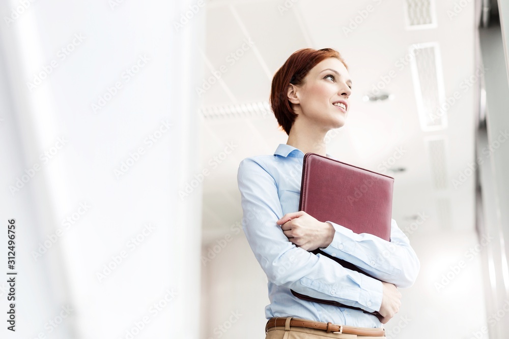 Thoughtful young businesswoman holding document while looking away at office Thoughtful young businesswoman holding document while looking away at office