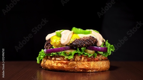 Craft burger is cooking on black background. Consist: red sauce salsa, lettuce, red onion, pickle, cheese, chilli green pepper, air bun and marbled meat beef. Not made ideal. Loving hand made. photo
