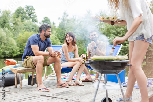 Low section of woman preparing food in barbecue grill with friends on pier