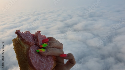 Woman eat sandwich and drinks tea and coffee in flight. Adventure on hot air balloon. Burner directing flame into envelope. Fly in morning blue sky above cloud. Girl stand in basket hot air balloon. photo