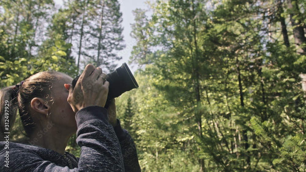 Traveler photographing scenic view in forest. One caucasian woman shooting nice magic look. Girl take photo video on dslr mirrorless camera. Professional photographer travel with backpack. Outdoor. Traveler photographing scenic view in forest. One caucasian woman shooting nice magic look. Girl take photo video on dslr mirrorless camera. Professional photographer travel with backpack. Outdoor.