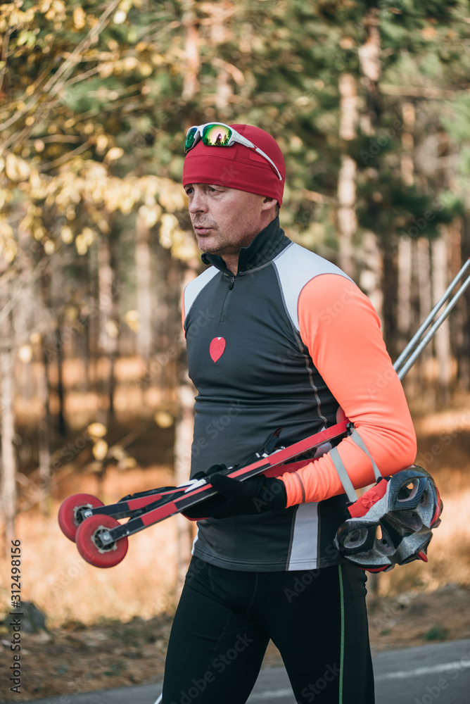 Training an athlete on the roller skaters. Biathlon ride on the roller skis with ski poles, in the helmet. Autumn workout. Roller sport. Adult man riding on skates. Training an athlete on the roller skaters. Biathlon ride on the roller skis with ski poles, in the helmet. Autumn workout. Roller sport. Adult man riding on skates.