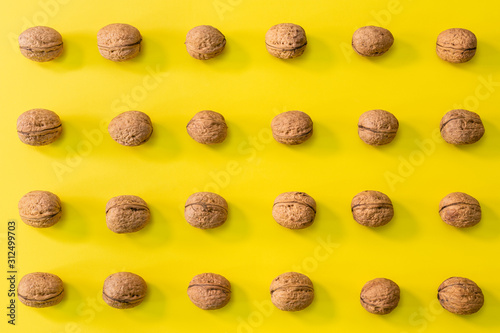 Walnuts in rows, minimalist pattern of walnuts on a bright bold yellow background, autumn food concept