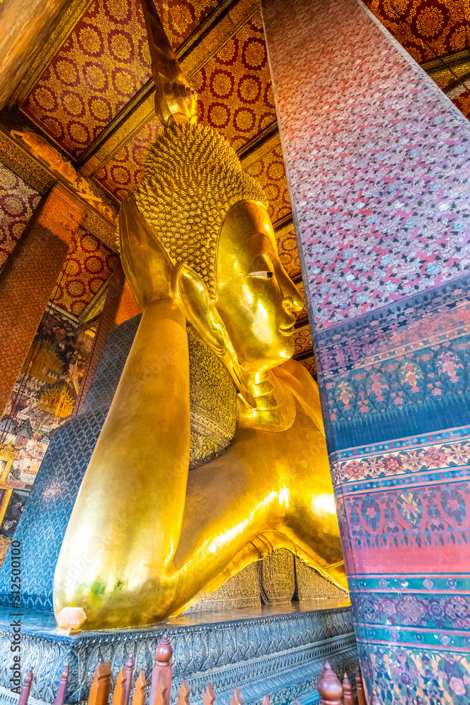 Beautiful statue of reclining golden Buddha placed in Wat Pho temple, Bangkok. Spiritual place of buddhism religion with beautiful ornaments on the pillar. Detail view of Buddha's head