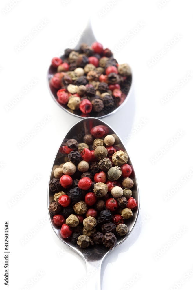Pepper grains on spoon on white background